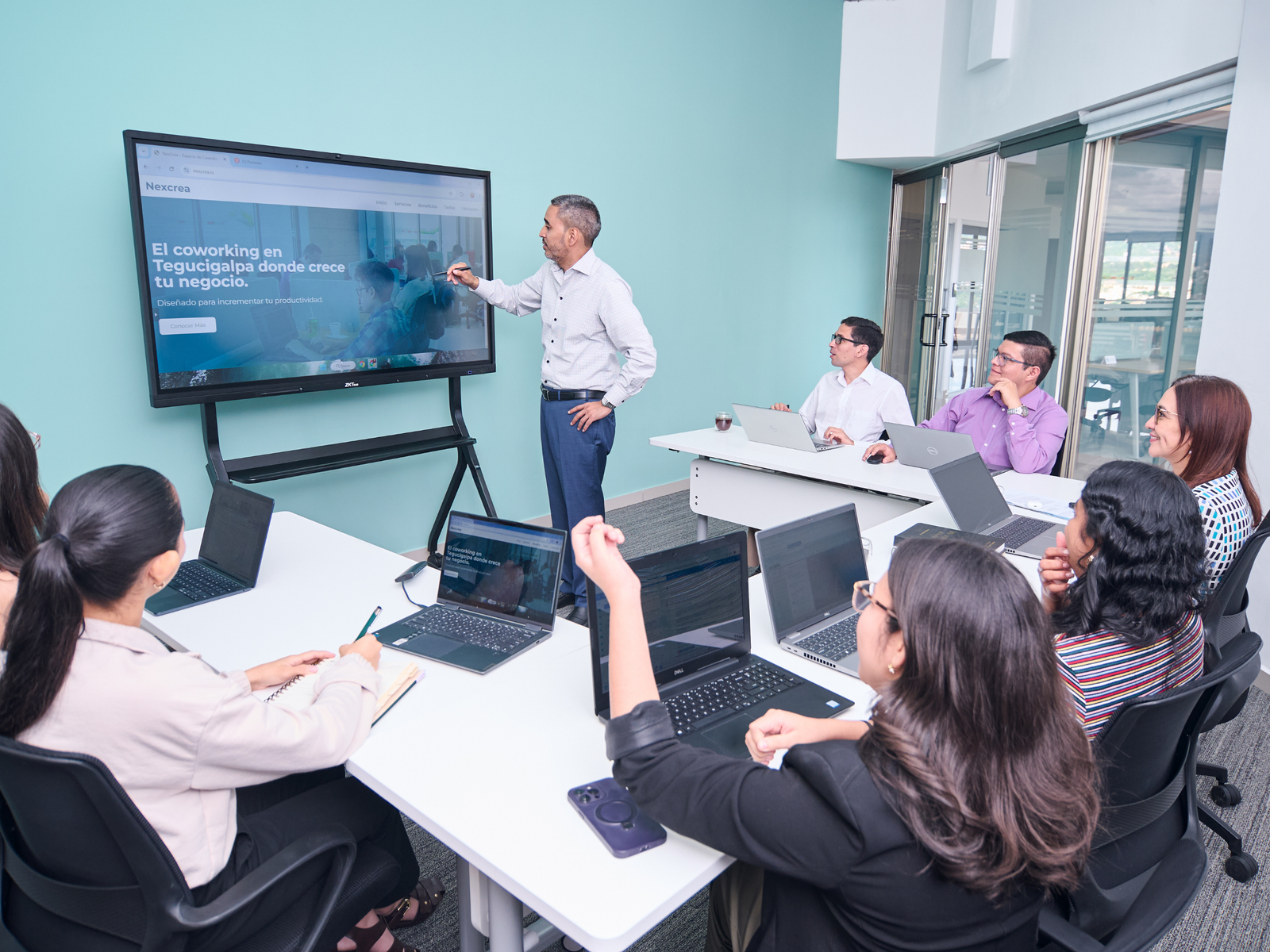 Consultor explicando una presentación en una pantalla ante un equipo profesional con laptops